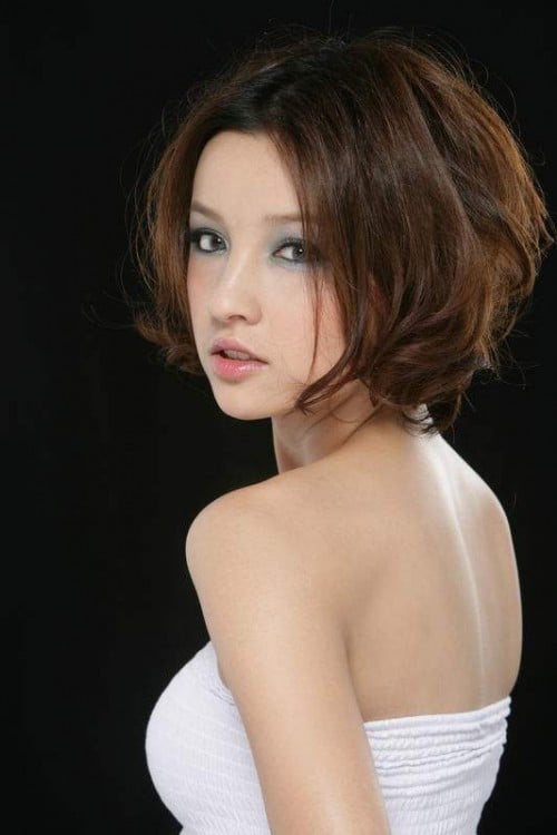A pretty Asian girl turned 3/4 away from the camera and looking back over her left shoulder. She has short black hair, and wears a white tube top exposing most of her back and shoulder. She wears heavy eye makeup which accentuates her eyes.
